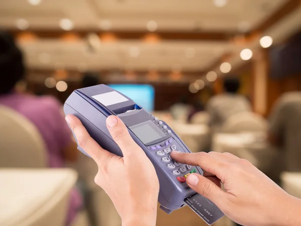 Hand Swiping Credit Card Machine with blurred people sitting rea — Stock Photo, Image