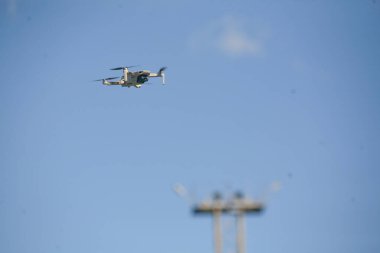 Küçük beyaz bir kuadkopter dron parlak mavi bir gökyüzüne karşı uçuyor soluk beyaz bir bulut ve bulanık bir ön plan yapısı ile