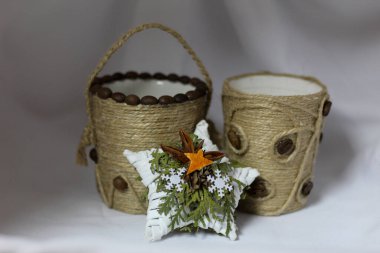 İki el yapımı konteynır jüt sicime sarılmış ve doğal tohumlarla süslenmiş. Önünde beyaz yıldız şeklinde bir süs, yeşillik ve kurutulmuş portakaldan yapılmış, sade bir çevre dostu tatil dekoru yaratıyor.