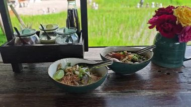 Yeşil pirinç tarlalarıyla çevrili kırsal bir restoranda servis edilen Tayland erişte yemekleriyle huzurlu bir kırsal bölge manzarası.