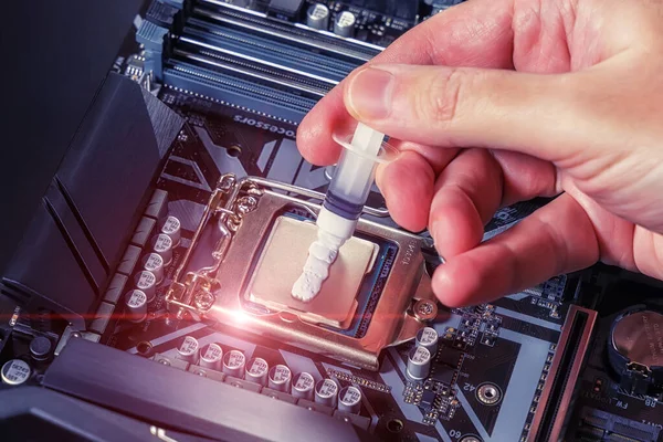 A technician applies white thermal paste to the CPU. Installing a cooler on a PC processor. Assembling or upgrading a Personal Computer
