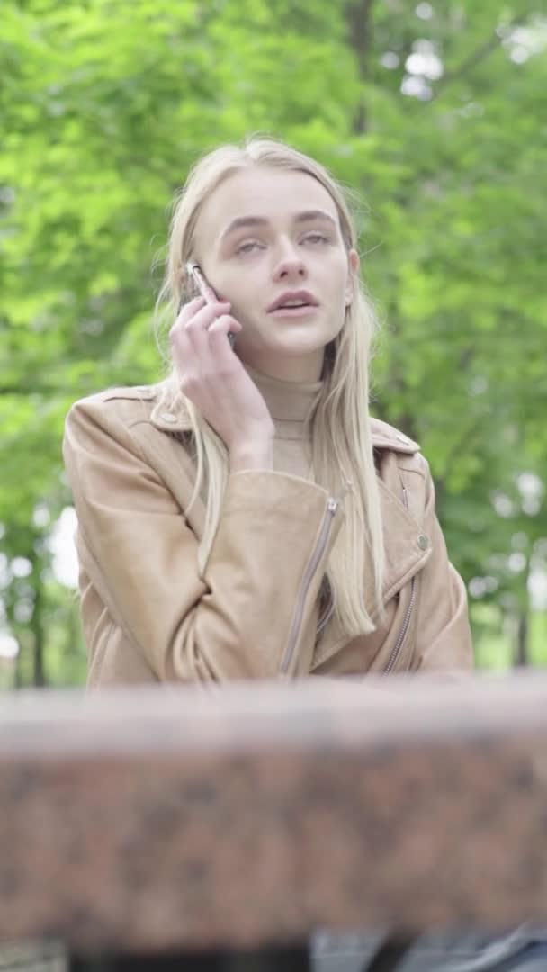 Vídeo vertical de una joven flaca en el parque. Chica con un teléfono móvil. — Vídeos de Stock