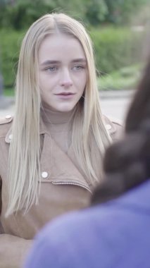 Parktaki genç, sıska bir kızın dikey videosu. Kız biriyle konuşuyor.