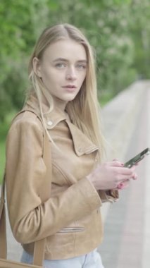 Parktaki genç, sıska bir kızın dikey videosu. Cep telefonu olan bir kız..