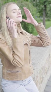 Parktaki genç, sıska bir kızın dikey videosu. Cep telefonu olan bir kız..