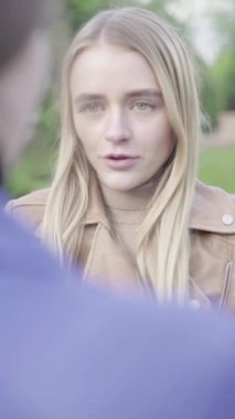 Parktaki genç, sıska bir kızın dikey videosu. Kız biriyle konuşuyor.