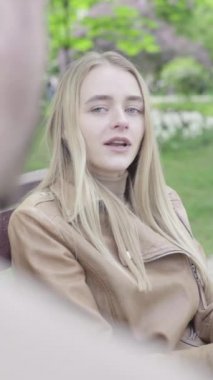 Parktaki genç, sıska bir kızın dikey videosu. Kız biriyle konuşuyor.