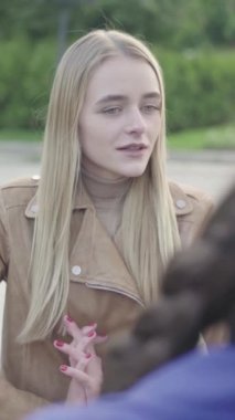 Parktaki genç, sıska bir kızın dikey videosu. Kız biriyle konuşuyor.