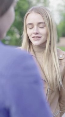 Parktaki genç, sıska bir kızın dikey videosu. Kız biriyle konuşuyor.