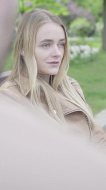 Parktaki genç, sıska bir kızın dikey videosu. Kız biriyle konuşuyor.