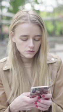 Parktaki genç, sıska bir kızın dikey videosu. Cep telefonu olan bir kız..