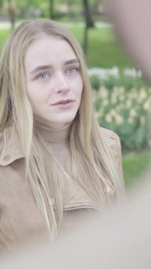 Parktaki genç, sıska bir kızın dikey videosu. Kız biriyle konuşuyor.