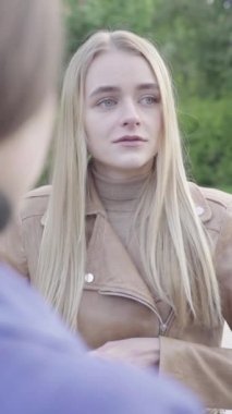 Parktaki genç, sıska bir kızın dikey videosu. Kız biriyle konuşuyor.