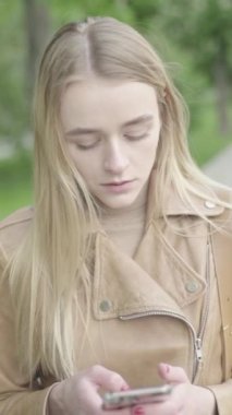 Parktaki genç, sıska bir kızın dikey videosu. Cep telefonu olan bir kız..