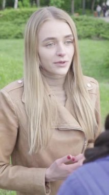 Parktaki genç, sıska bir kızın dikey videosu. Kız biriyle konuşuyor.