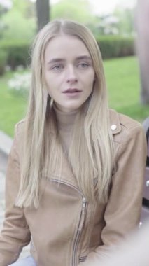 Parktaki genç, sıska bir kızın dikey videosu. Kız biriyle konuşuyor.