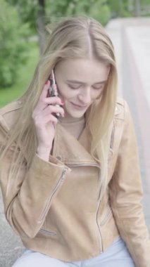 Parktaki genç, sıska bir kızın dikey videosu. Cep telefonu olan bir kız..