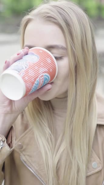 Vertical video of a young skinny girl in the park. The girl is drinking coffee. — Stock Video