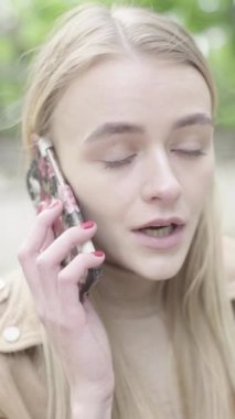 Parktaki genç, sıska bir kızın dikey videosu. Cep telefonu olan bir kız..