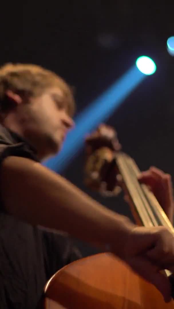 男のチェリストが暗闇の中でチェロを演奏する。垂直ビデオ — ストック動画