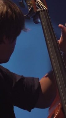 Erkek çellocu, karanlıkta sahnede çello çalıyor. Dikey video