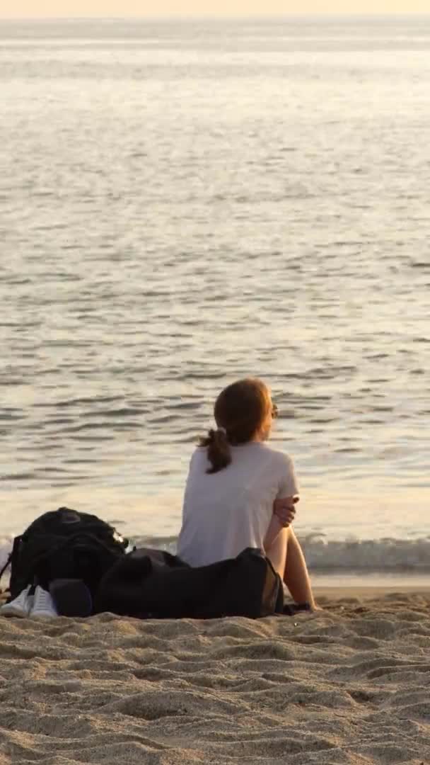 Flicka som sitter vid havet på sanden Vertikal video — Stockvideo