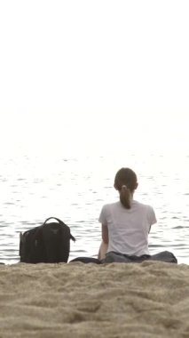 Kumun üzerinde deniz kenarında oturan kız dikey video