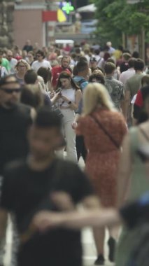Şehir caddesi boyunca kalabalık içinde yürüyen bir sürü insanın dikey videosu.