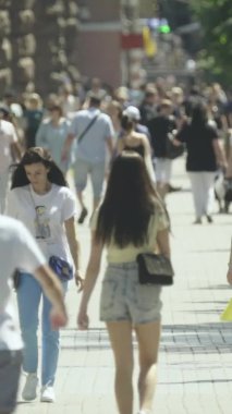 Şehir caddesi boyunca kalabalık içinde yürüyen bir sürü insanın dikey videosu.