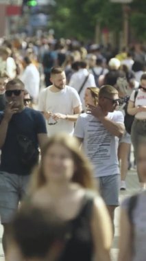 Şehir caddesi boyunca kalabalık içinde yürüyen bir sürü insanın dikey videosu.
