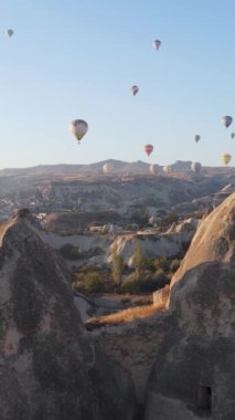 Türkiye 'nin Kapadokya üzerinde gökyüzünde uçan sıcak hava balonlarının dikey videosu.