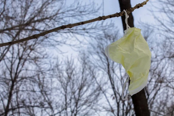 A used medical mask hangs on a tree branch. Pollution of nature with protective masks. Ecological problem. Coronavirus protection.