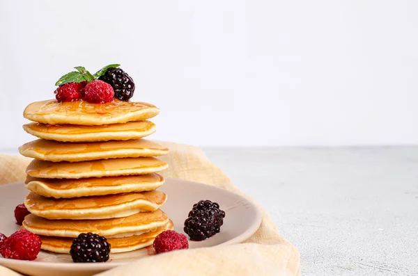 Homemade classic American pancakes with fresh raspberries, blackberries, honey and mint leaves, on a light background. — Stock Photo, Image