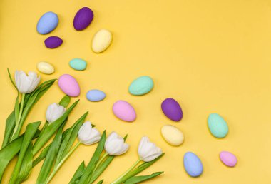 Sarı arka planda bir buket beyaz lale olan renkli Paskalya yumurtaları. Bahar konsepti, metin yeri, kopyalama alanı, düz yatak. Pankart. Yukarıdan görüntüle.