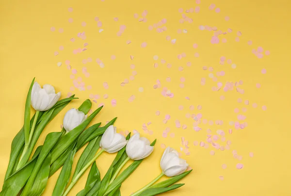 Bouquet of white tulips with pink confetti on a yellow background. Spring concept, place for text, copy space, flat lay. Banner. View from above