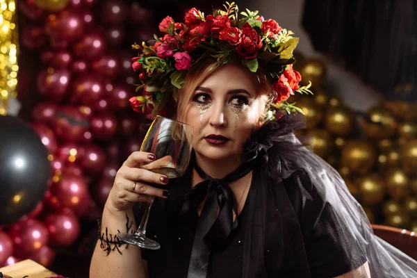 Mooie vrouw in elegante zwarte jurk met een glas wijn vieren verjaardag, Halloween. Een volwassen heks in een kamer versierd voor Halloween — Stockfoto