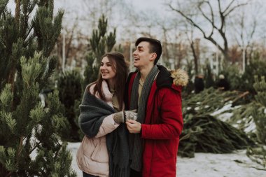 Güzel, beyaz, heteroseksüel bir çift alışverişçi kışın açık havada, karlı havada Noel ağacı pazarından alışveriş yapıyor.