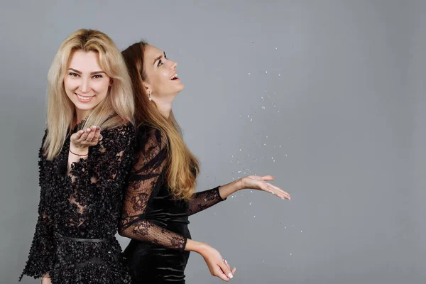 Kerstmis aan het vieren. Twee jonge vrouwen gooien zilveren lovertjes en confetti in de lucht in de studio. Feesttijd — Stockfoto