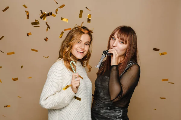 Twee jonge vrouwen op een beige achtergrond met gouden confetti hebben plezier en vieren kerst — Stockfoto