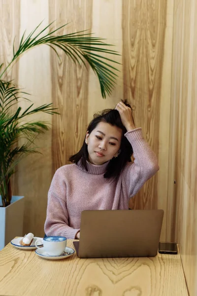 Menina adulta bonito joga em um laptop em uma cafeteria. Mulher asiática trabalhando em um café em um laptop. Conceito freelance — Fotografia de Stock