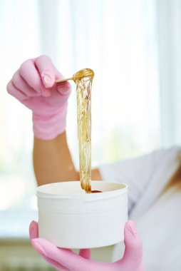 Kozmetik uzmanı şeker ezmesi çekiyor. Eli epilasyon macunu tutuyor.