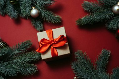 Noel ağacı dalları ve toplarının yanında kırmızı saten bir kurdele ve kırmızı arka planda oyuncaklar olan bir el işi hediyesi.