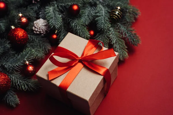 Caja de regalo con lazo rojo y ramita de árbol de Navidad sobre fondo rojo. Estilo laico plano. Concepto de celebración de Navidad o Año Nuevo —  Fotos de Stock