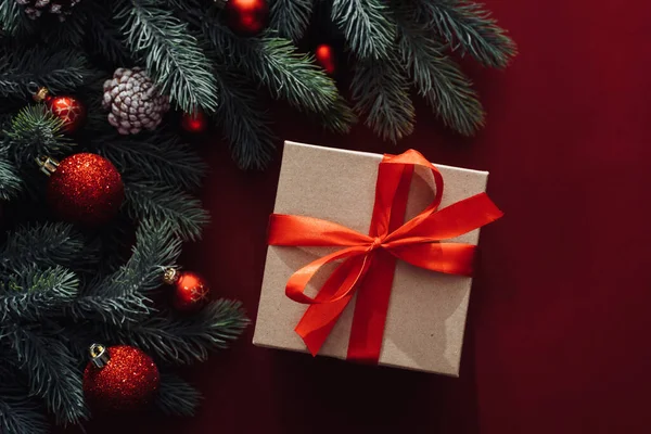 Kırmızı fiyonklu hediye kutusu ve kırmızı arka planda Noel ağacı dalı. Düz yatış stili. Noel veya Yeni Yıl Kutlama Konsepti