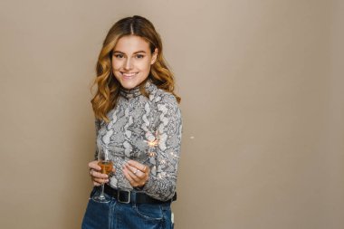 Samimi gülüşü olan genç bir kadın kameraya bakar, yanan Noel fişekleriyle poz verir ve şampanya içer. Tatil kutlaması konsepti