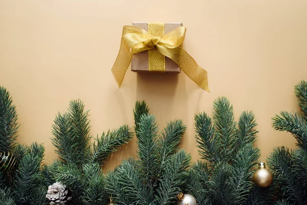 Dárková krabice se zlatým lukem a vánoční stromeček s kuličkami na béžovém pozadí. Plochý styl. Vánoční nebo novoroční koncepce oslav — Stock fotografie