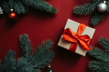 Kırmızı fiyonklu hediye kutusu ve kırmızı arka planda topları olan Noel ağacı dalı. Düz yatış stili. Noel veya Yeni Yıl Kutlama Konsepti