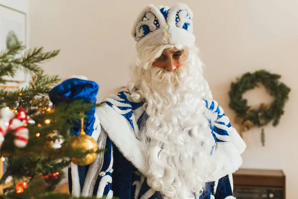 Der Weihnachtsmann im blauen Pelzmantel im weihnachtlichen Interieur schmückt einen Weihnachtsbaum — Stockfoto