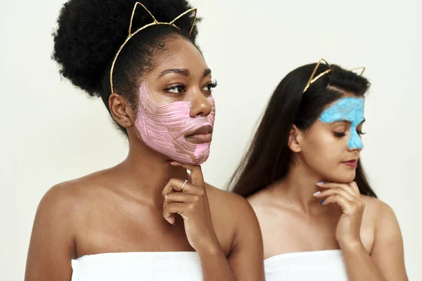 Twee vriendinnen of verliefde jonge vrouwen proberen zichzelf te maskeren. Spa dag. Een foto van twee meisjes vrienden ontspannen met gezichtsmaskers op meer dan witte achtergrond — Stockfoto