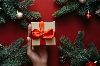 Kadın elleri hediye kutusunu tutuyor. Firavun ağacı ve tatil süslemeleri. Yeni yıl tatili konsepti. Düz yerde, üst tarafta. Mutlu Noeller kartı.